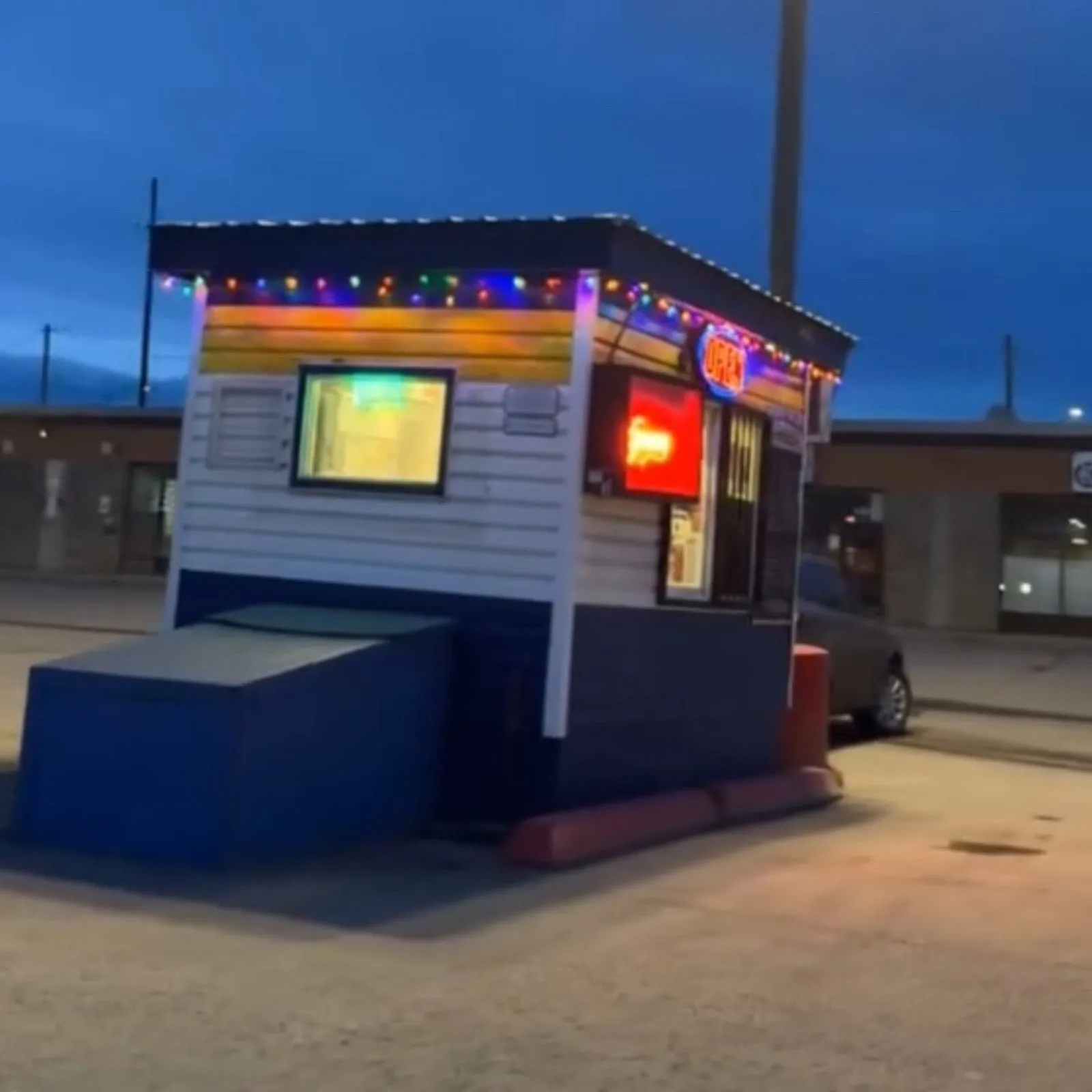 The original blue and white VV's hut at dusk with a neon OPEN sign lit in the window